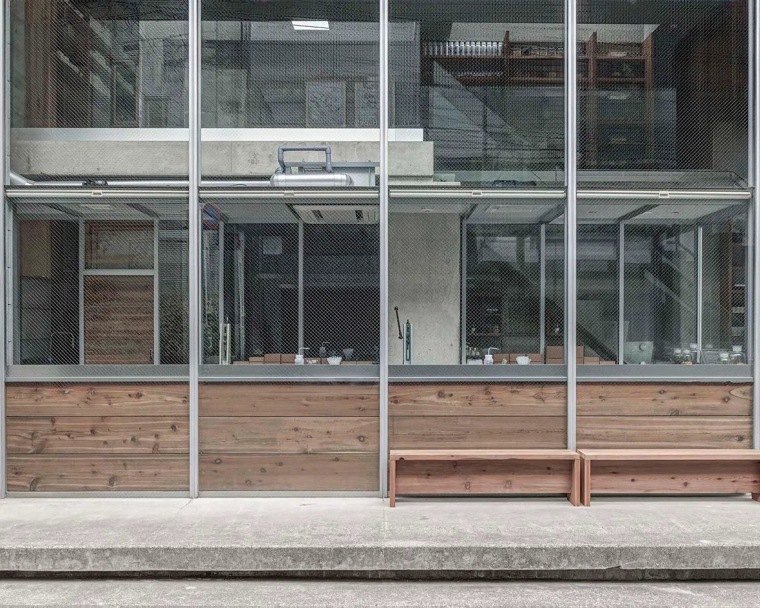 A modern building with a large glass wall and two benches inside, surrounded by natural light
