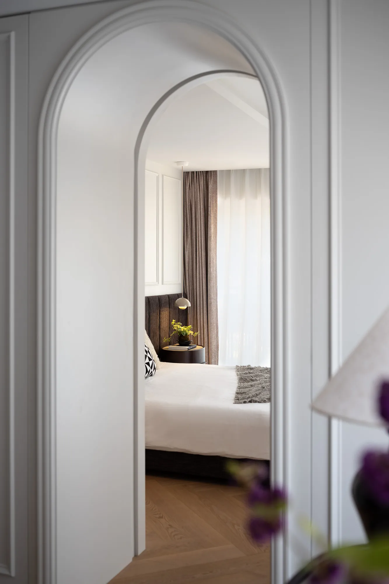 Cozy bedroom with a white bed, black pillows, and ample lighting from two lamps and large windows