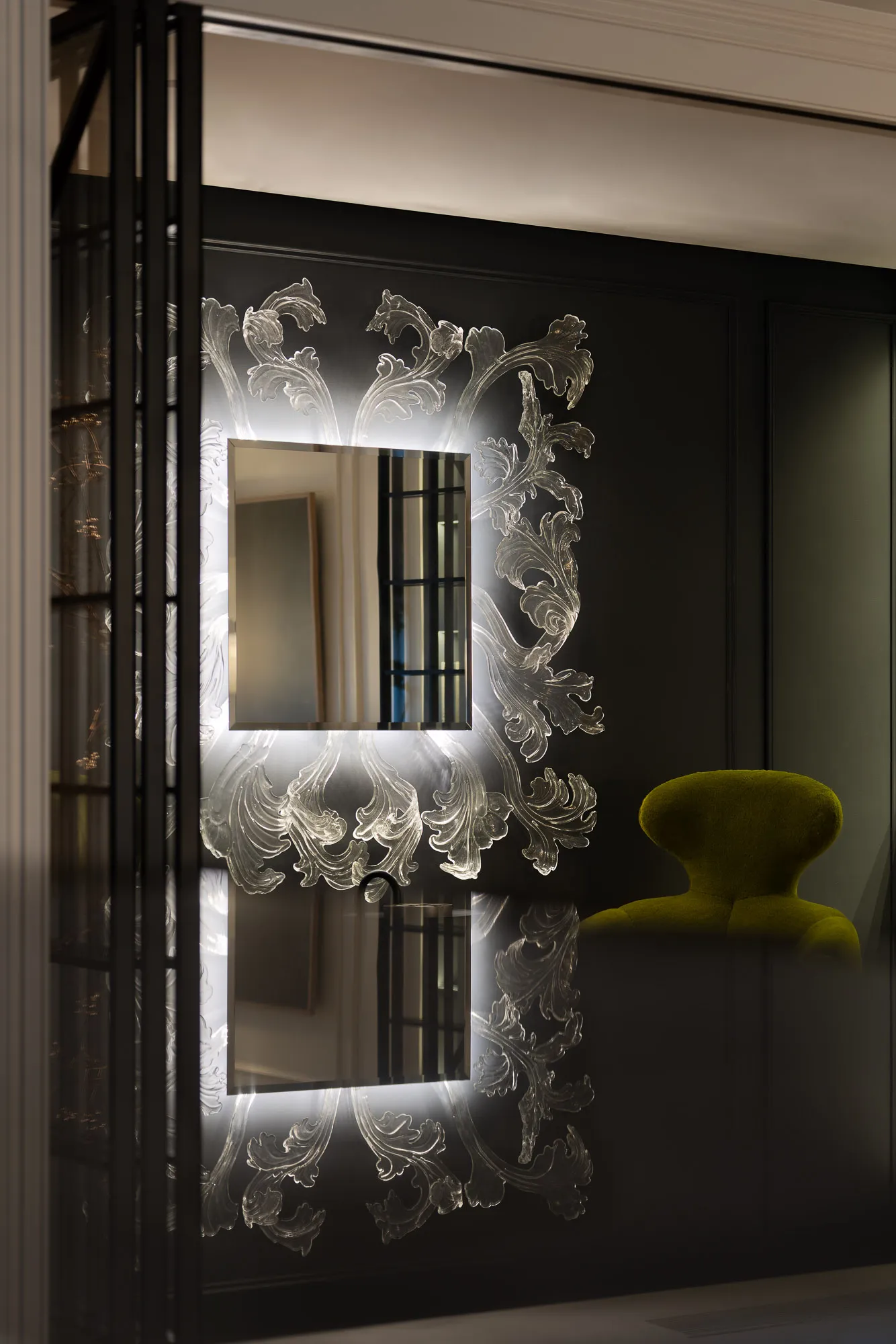 A modern living area with a green chair and ornate mirror, set against a black wall