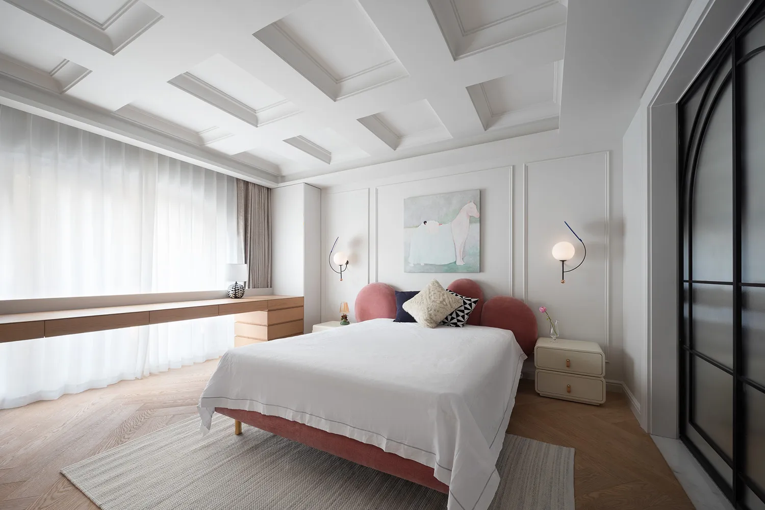 A calm and inviting bedroom with a large white bed, pink headboard and footboard, two nightstands with lamps, a couch, and a chair
