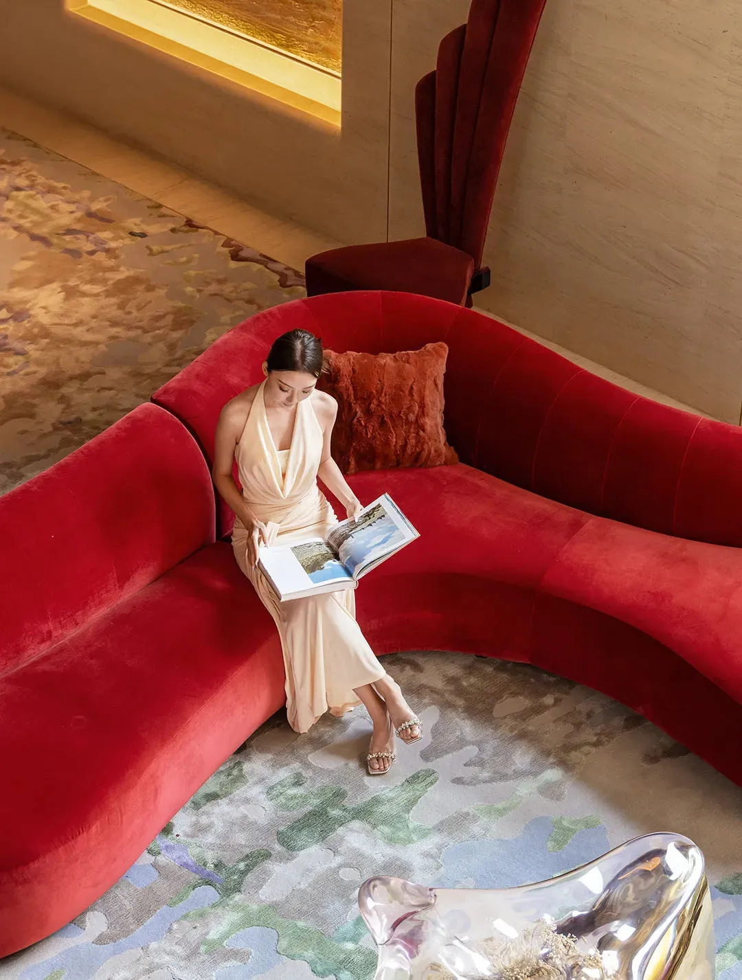 A woman sits on a red couch in a peaceful living room with a carpeted floor, surrounded by a calm atmosphere