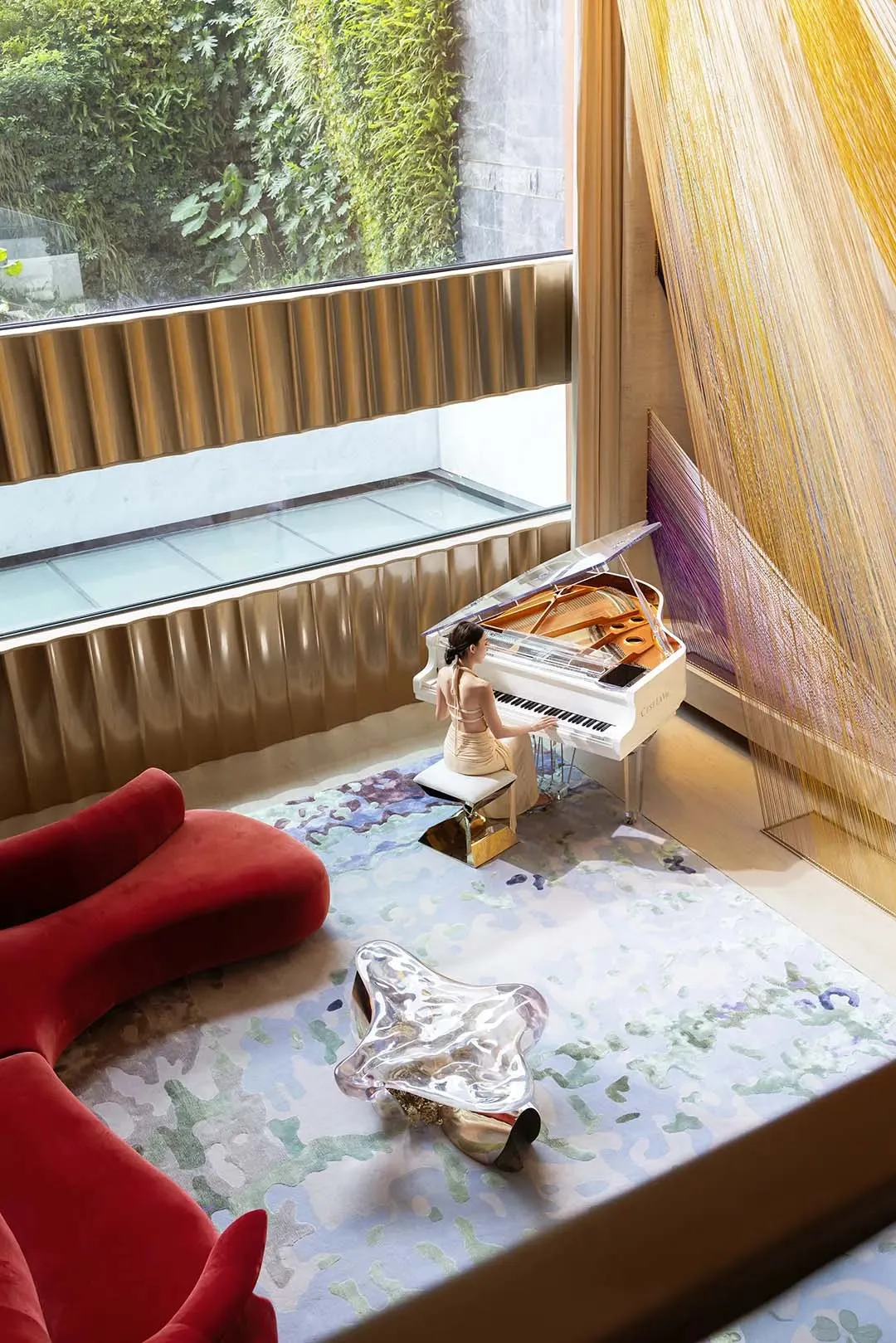 A woman plays the piano in a cozy living area with a grand piano, couches, and chairs, creating a warm and inviting atmosphere