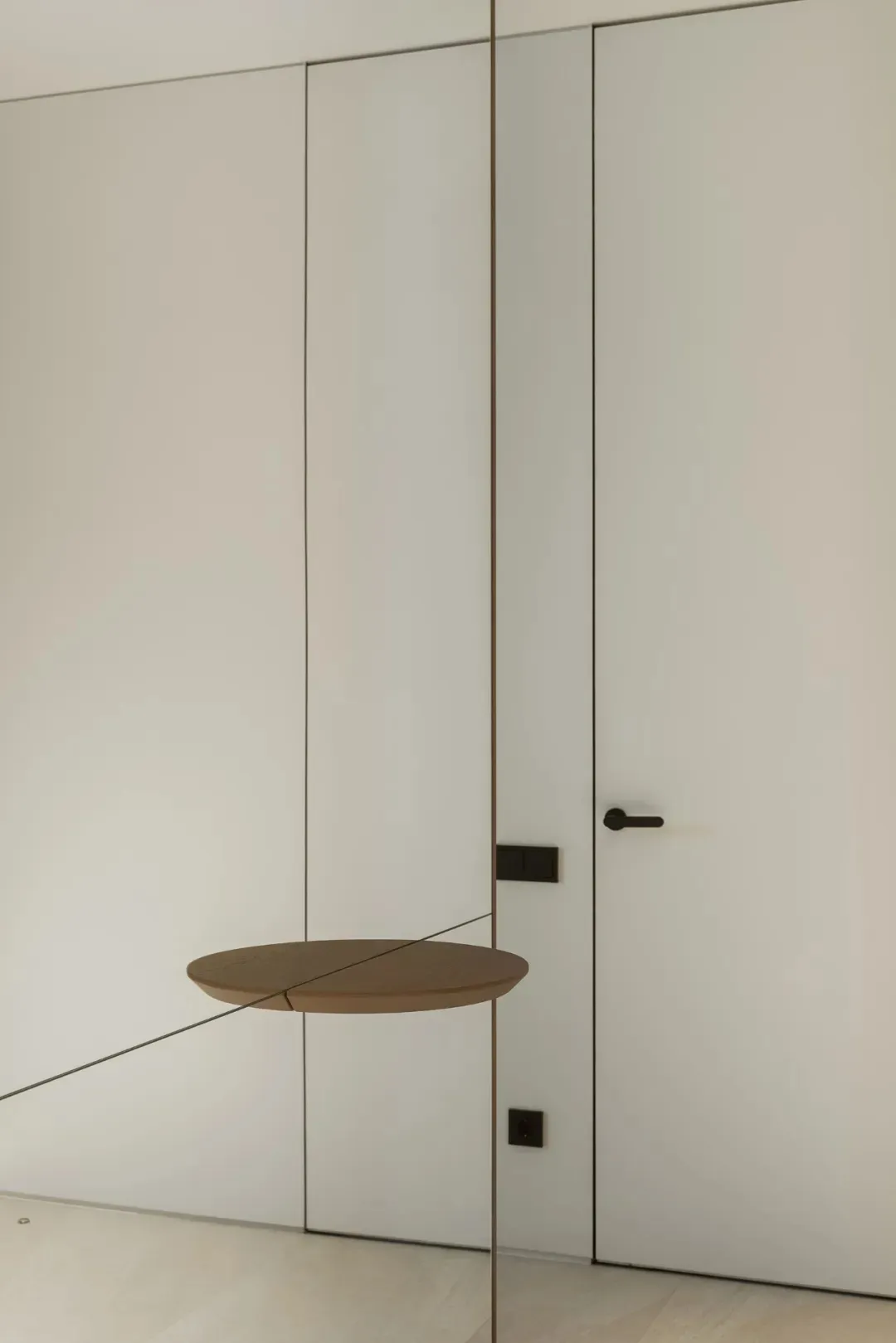 A white room with a brown door, a mirror, and a decorative piece above the door, creating a clean and minimalistic atmosphere
