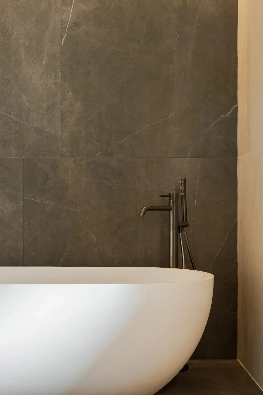 A modern bathroom with a large white bathtub in front of a gray wall, featuring two faucets and an elegant design