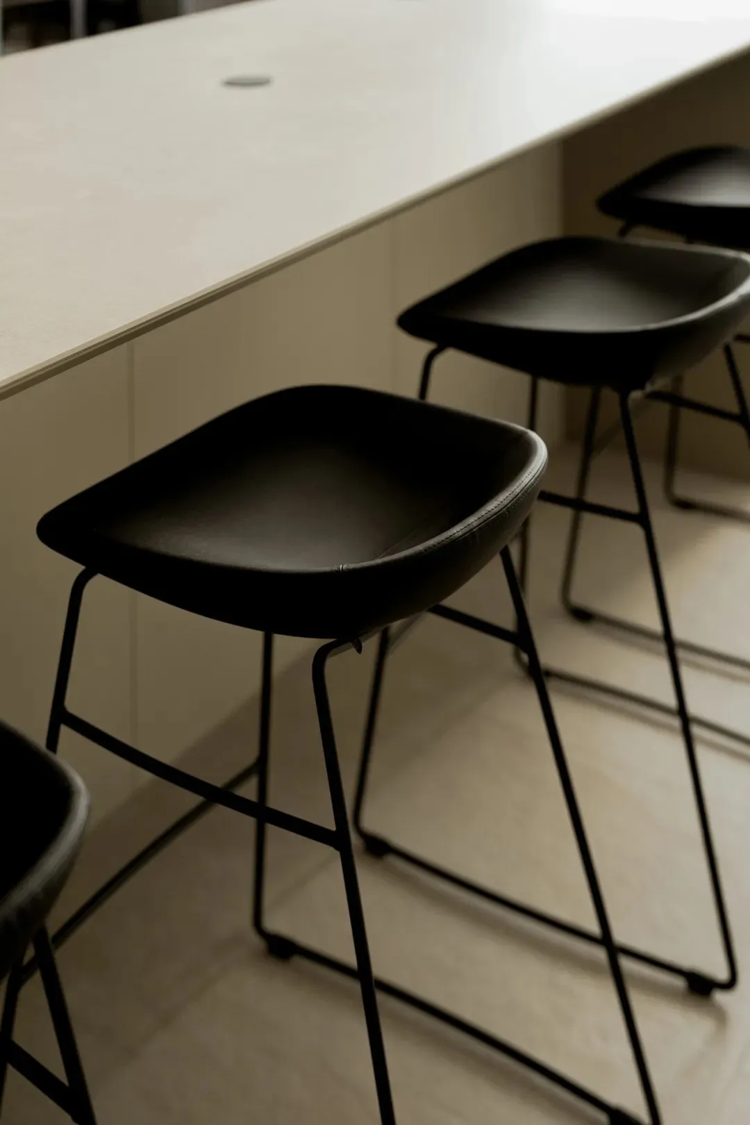 Empty kitchen space with four black stools around a marble countertop island, creating a casual dining atmosphere