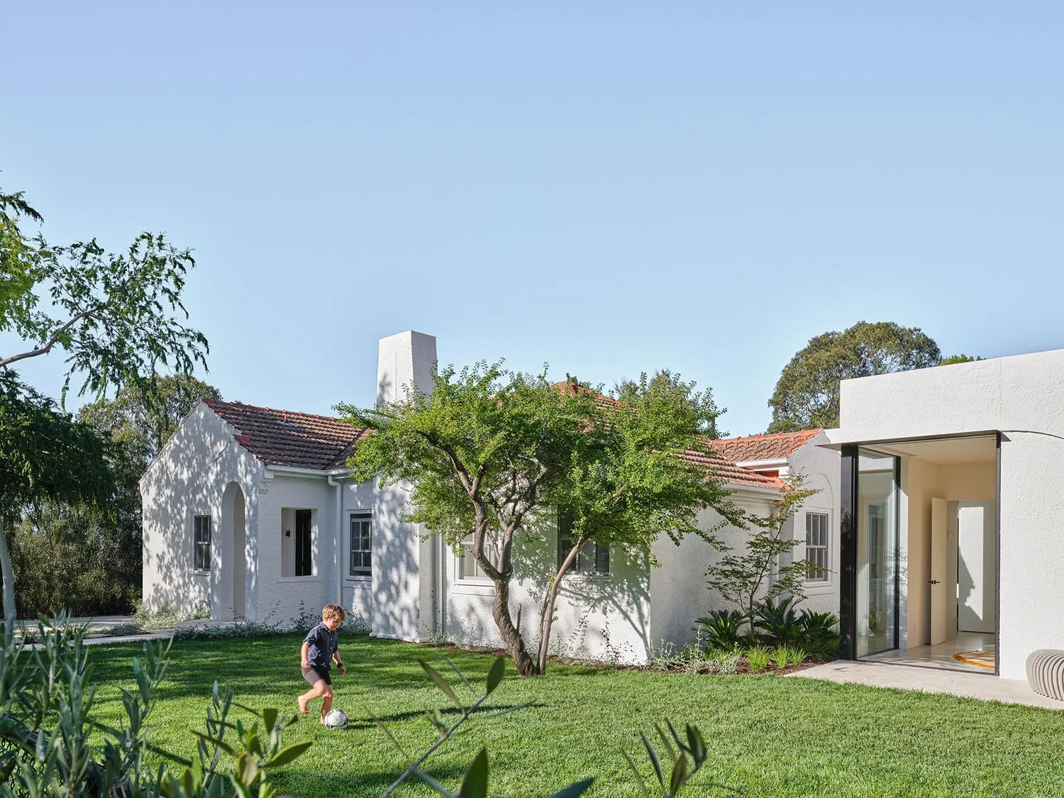 A white house with a green lawn and a patio with a dining table and chairs, surrounded by a relaxed family-oriented atmosphere