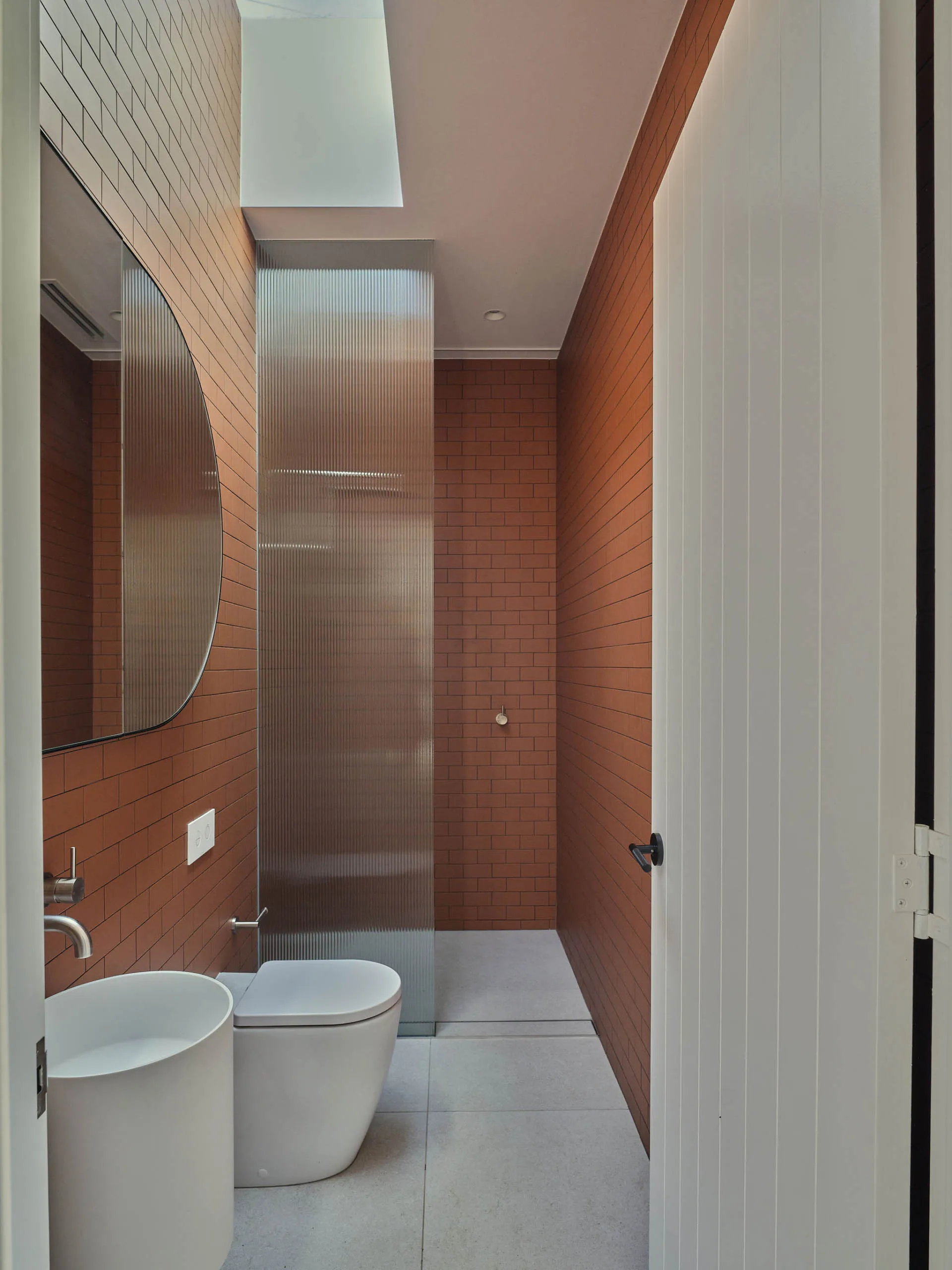 Bathroom with two sinks and a toilet, featuring brown brick walls and a warm atmosphere