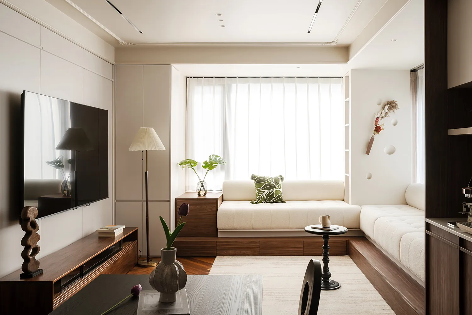 A modern living area with a white couch, wooden furniture, and a dining table near a window, filled with natural light