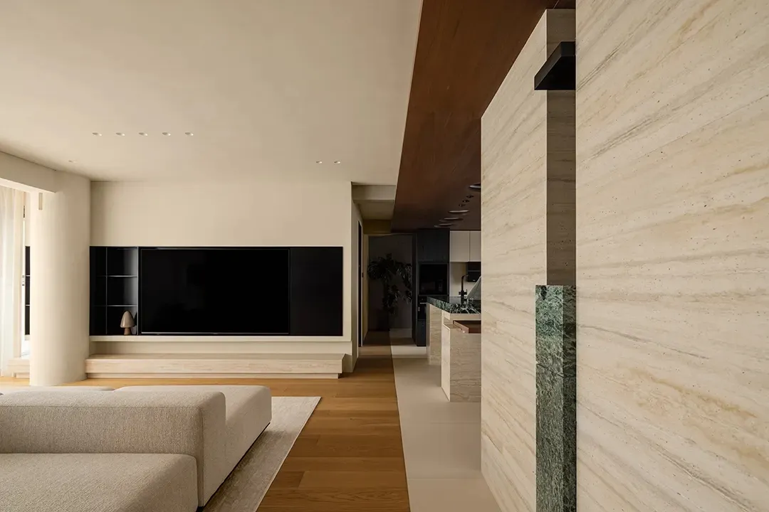 Open living area with wooden floors, neutral tones, and a large flat screen TV, featuring two couches and a potted plant