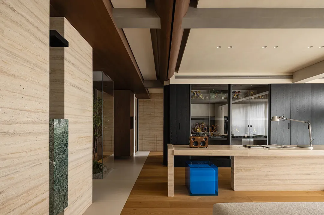 Open modern living space with a wooden table, chairs, couch, and additional seating, surrounded by potted plants and well-lit