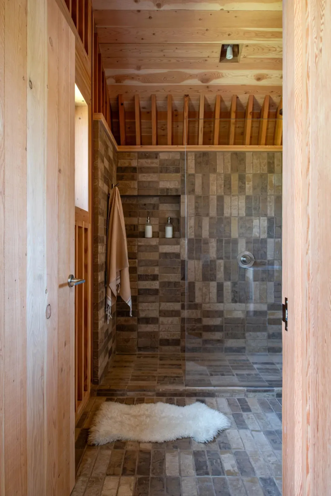Clean and organized bathroom with a modern shower stall featuring a glass door and a tiled design, with two bottles on the edge