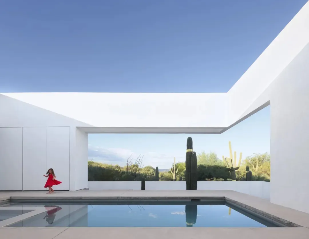 A modern indoor pool area with a large pool surrounded by white walls and potted plants, creating a serene ambiance