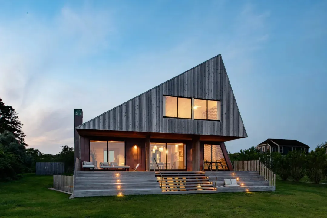A modern house with a triangular shape, featuring large windows, wooden exterior walls, and a warm and inviting atmosphere