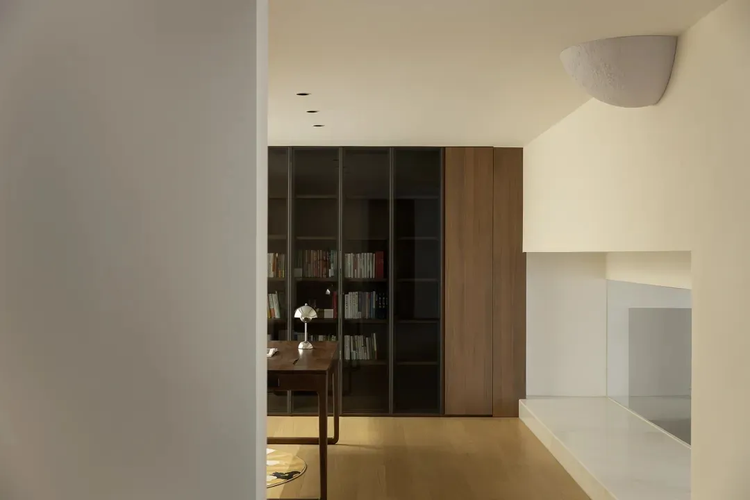 A warm and inviting living space with wooden floors, white walls, bookshelves, a dining table, and a chair, perfect for relaxation and socializing