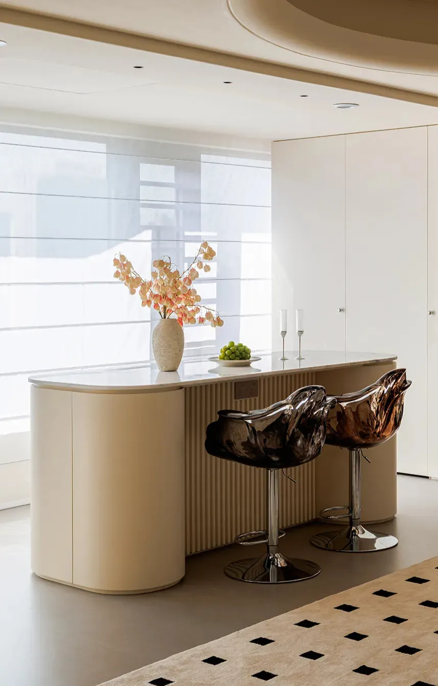Modern kitchen with white cabinets and countertops, two chairs, a vase with flowers, and wine glasses on the counter