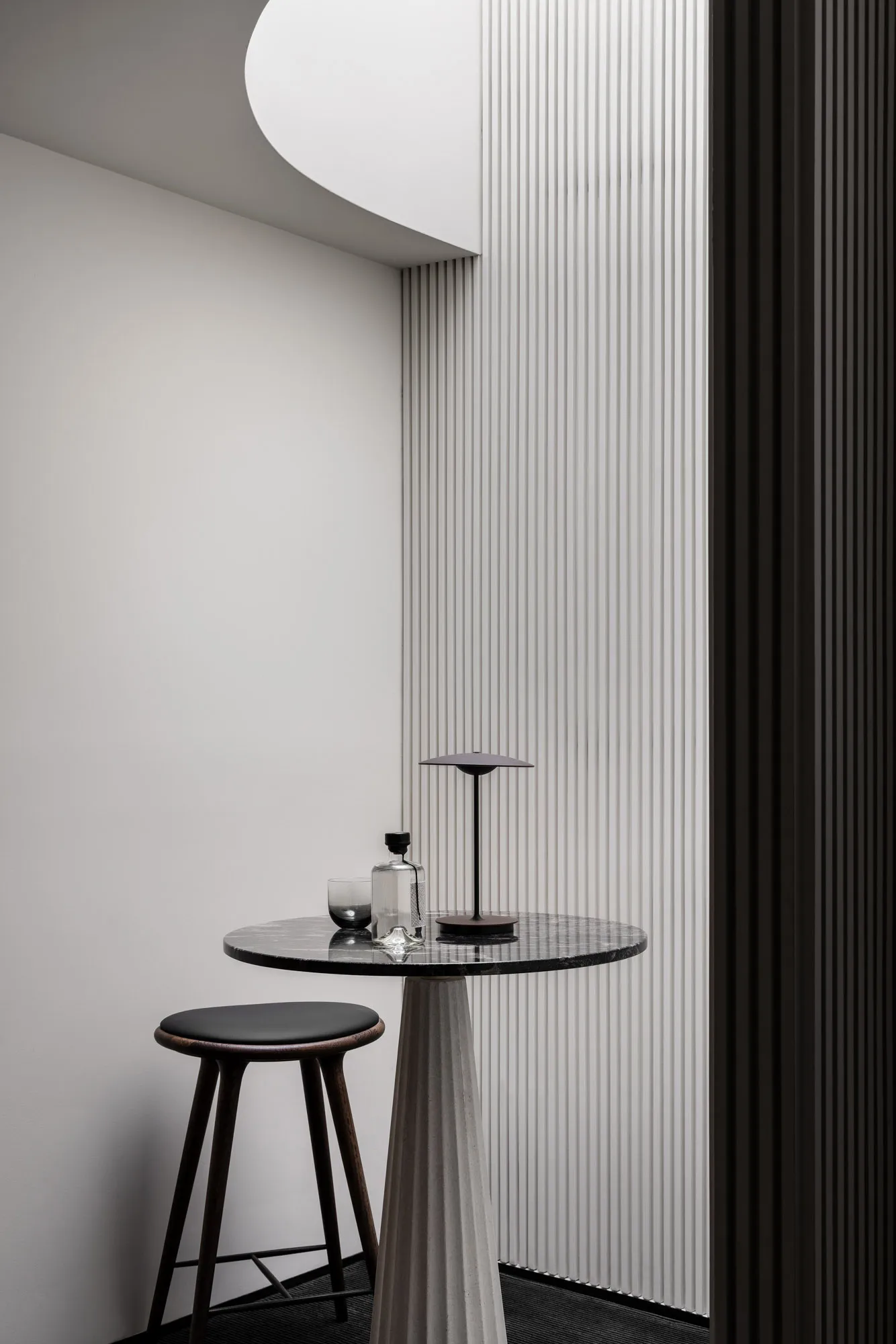 A small table with a vase sits in front of a striped wall, surrounded by two chairs in an elegant and well-organized interior design space