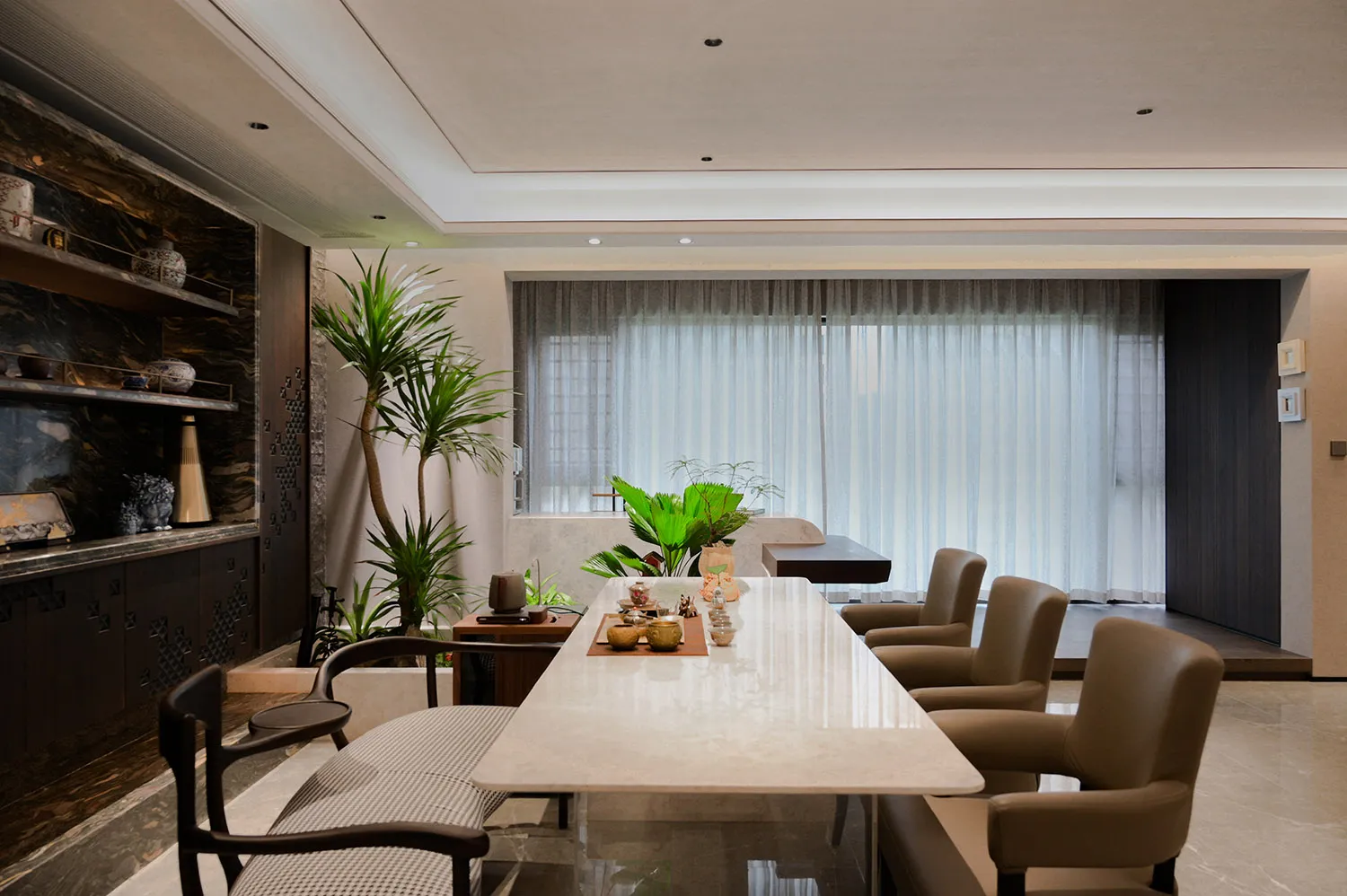 Open modern living area with a dining table, chairs, potted plants, a couch, and a chair, featuring a modern design and inviting ambiance