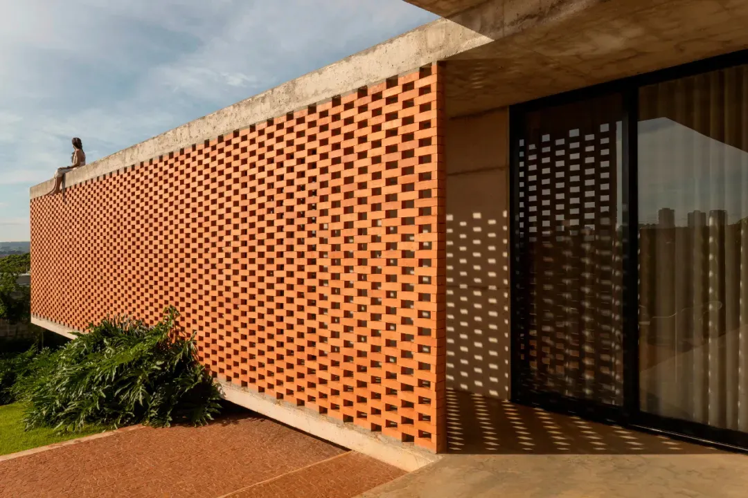 A modern architectural building with a unique checkered pattern on its exterior wall, made of orange bricks, with windows suggesting interior spaces