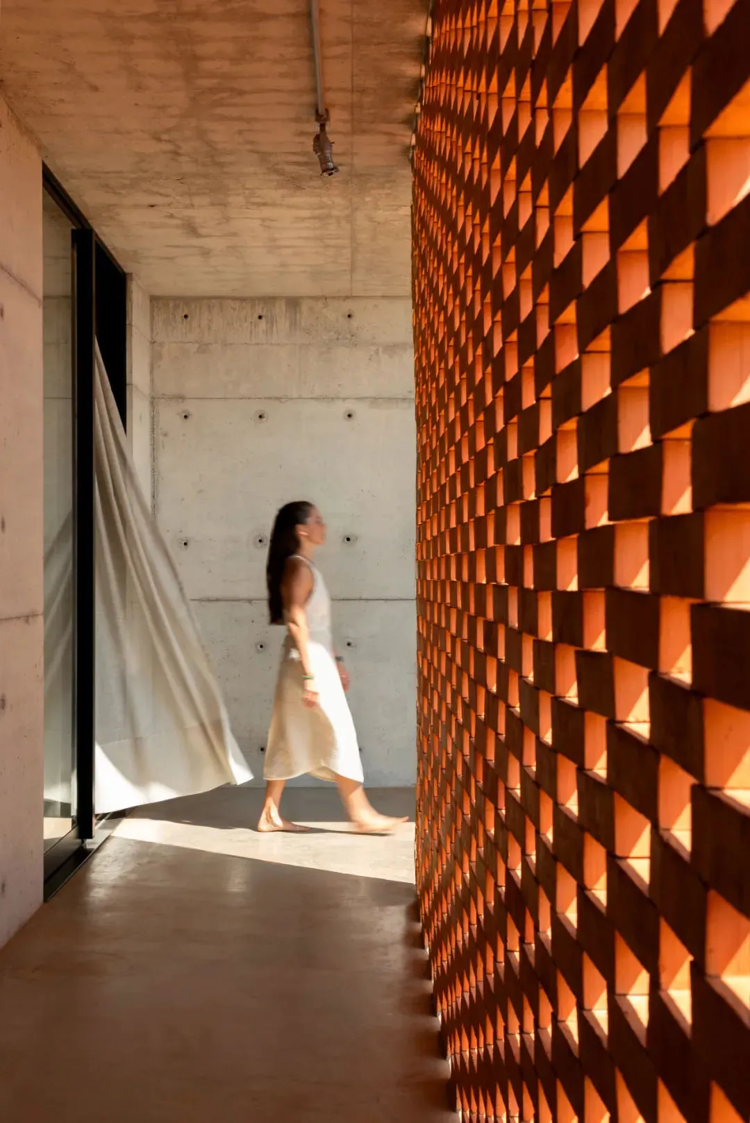 A woman walks through a modern space with concrete walls, minimalist design, and a calm atmosphere