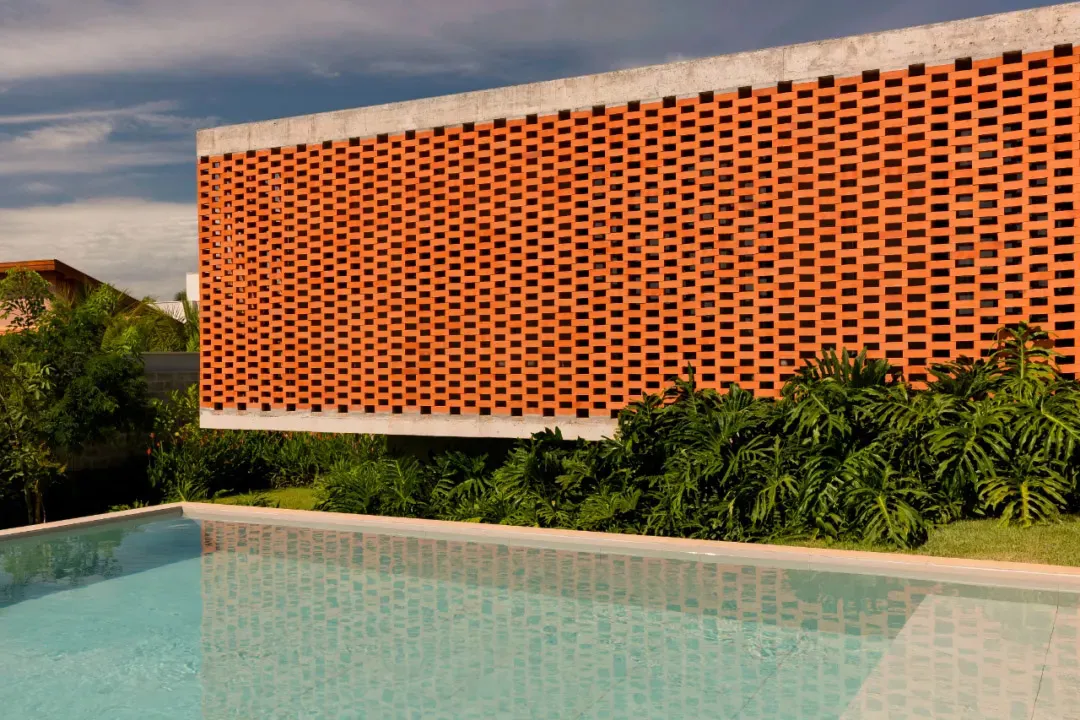 A brick wall with a textured appearance stands in front of a pool area with a reflective surface, creating a relaxing atmosphere