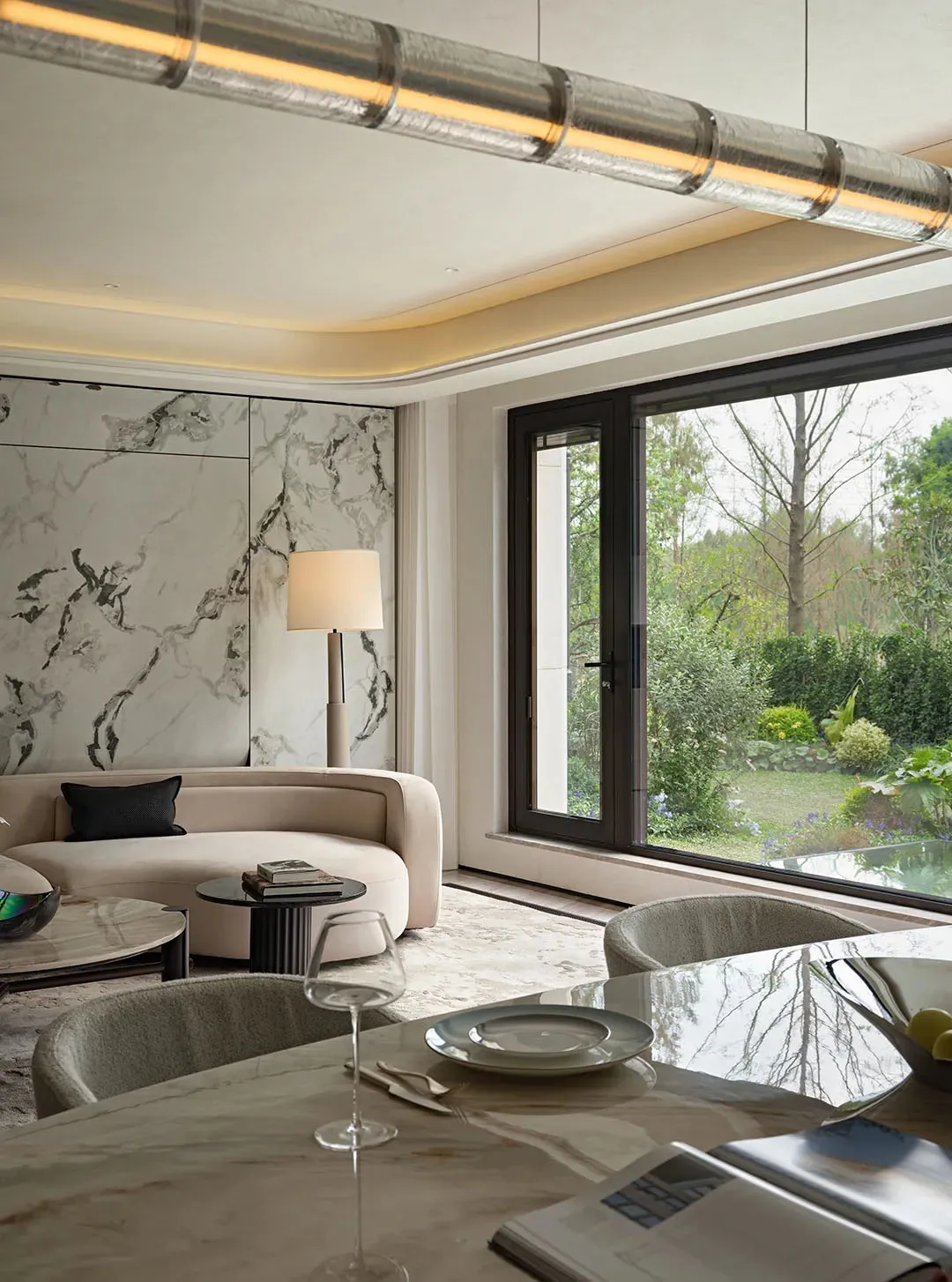 Modern living room with two couches, a dining table, and decorative elements, flooded with natural light from a large window