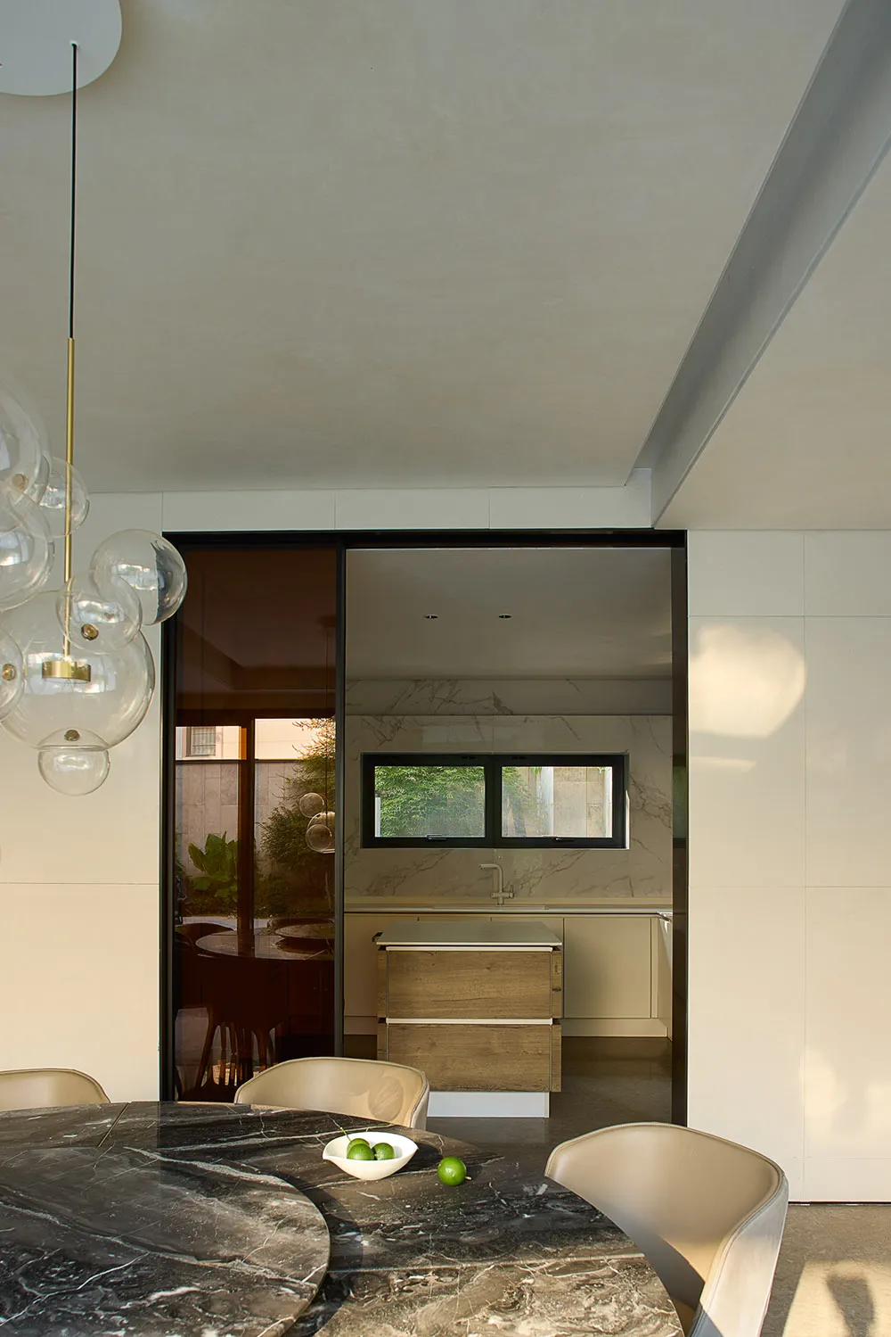 A well-lit kitchen with white walls, a black door, a dining table, chairs, and a refrigerator, creating a bright and inviting atmosphere