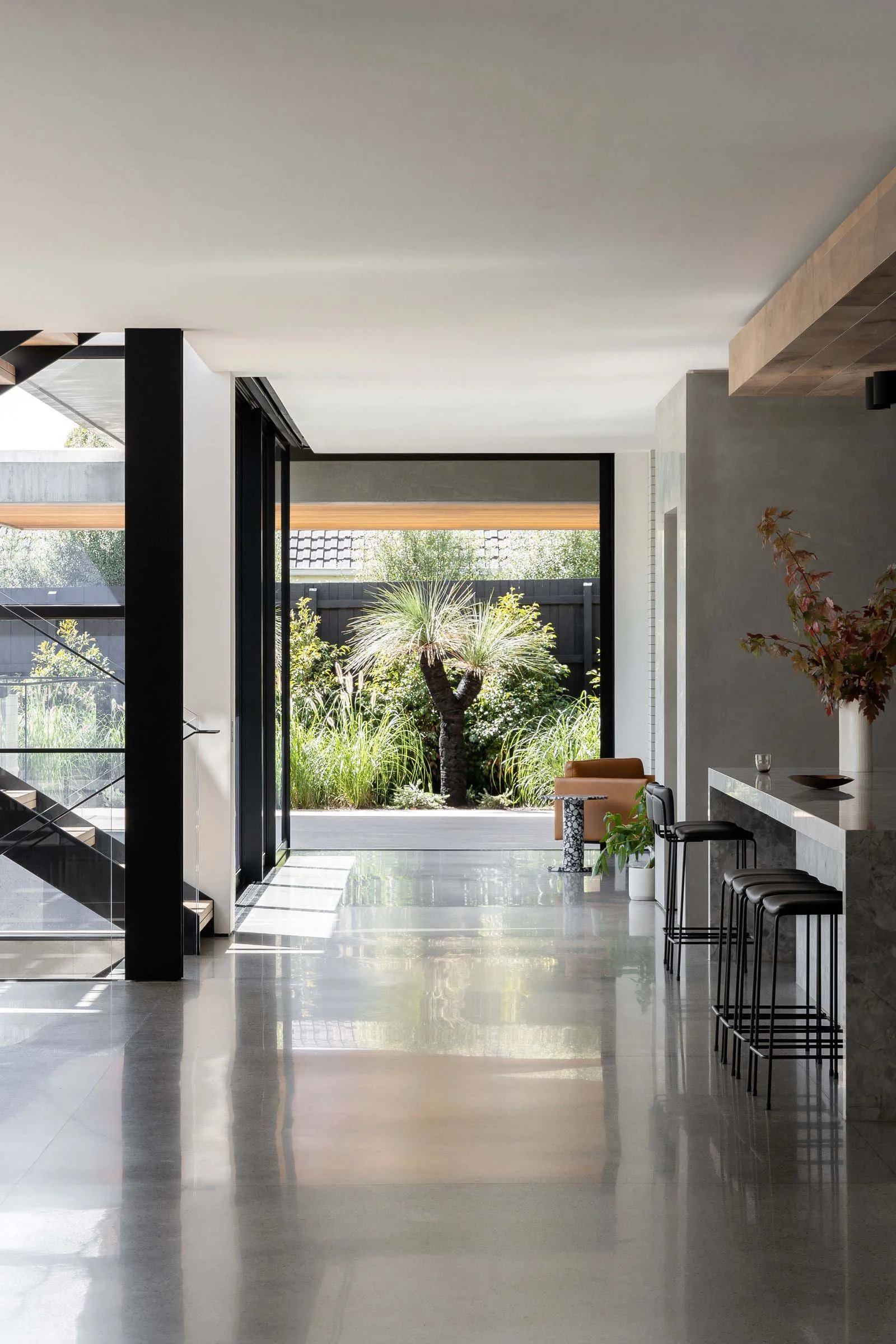 Modern open plan living area with white walls and floors, featuring a kitchen, dining room, and living room with two chairs and a dining table