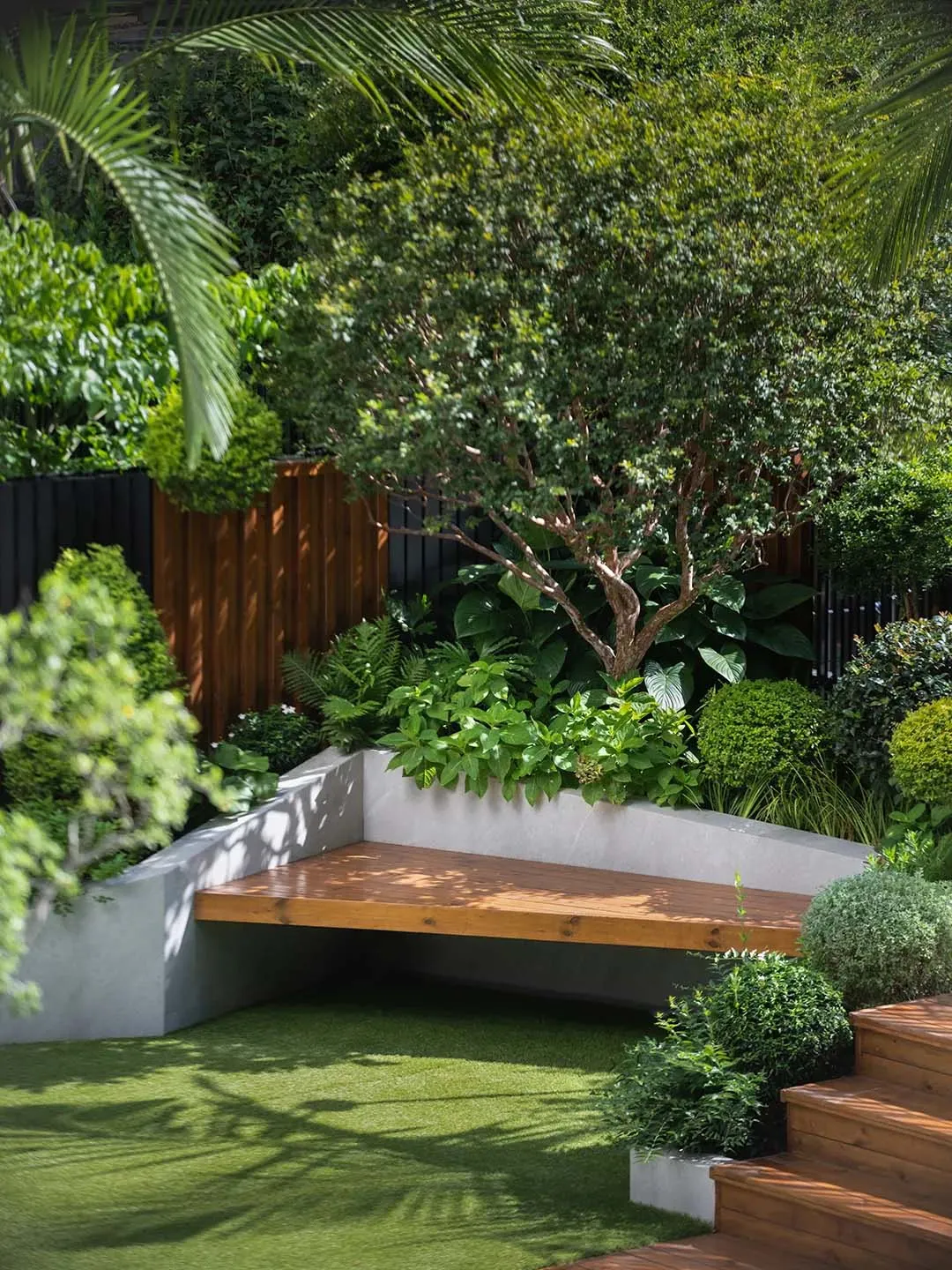 A wooden bench surrounded by greenery and potted plants, with a fence and two bottles in a relaxing outdoor patio setting