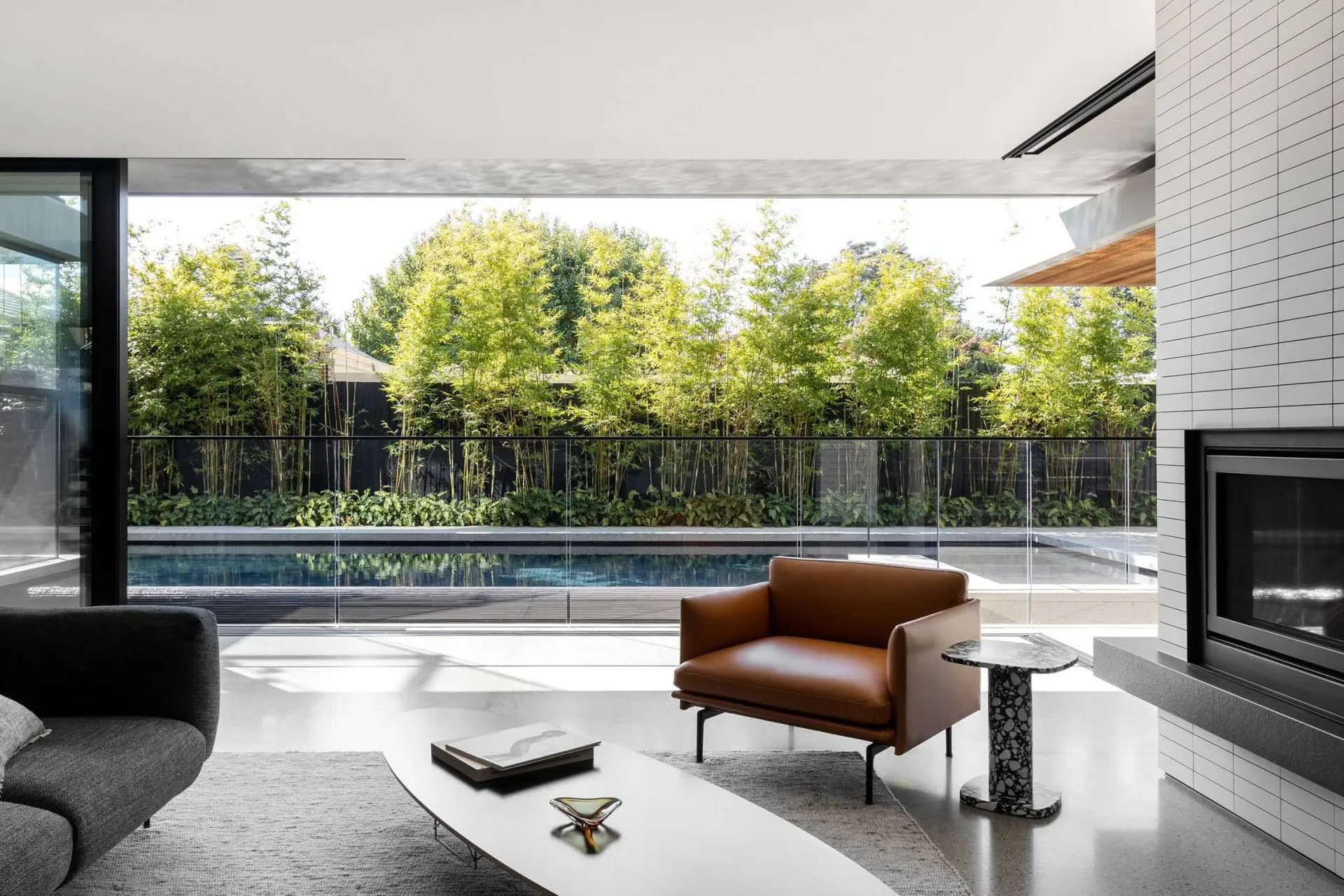 Modern living room with two couches, a chair, and a large window overlooking a pool area, featuring white walls and grey flooring, with natural light filling the space