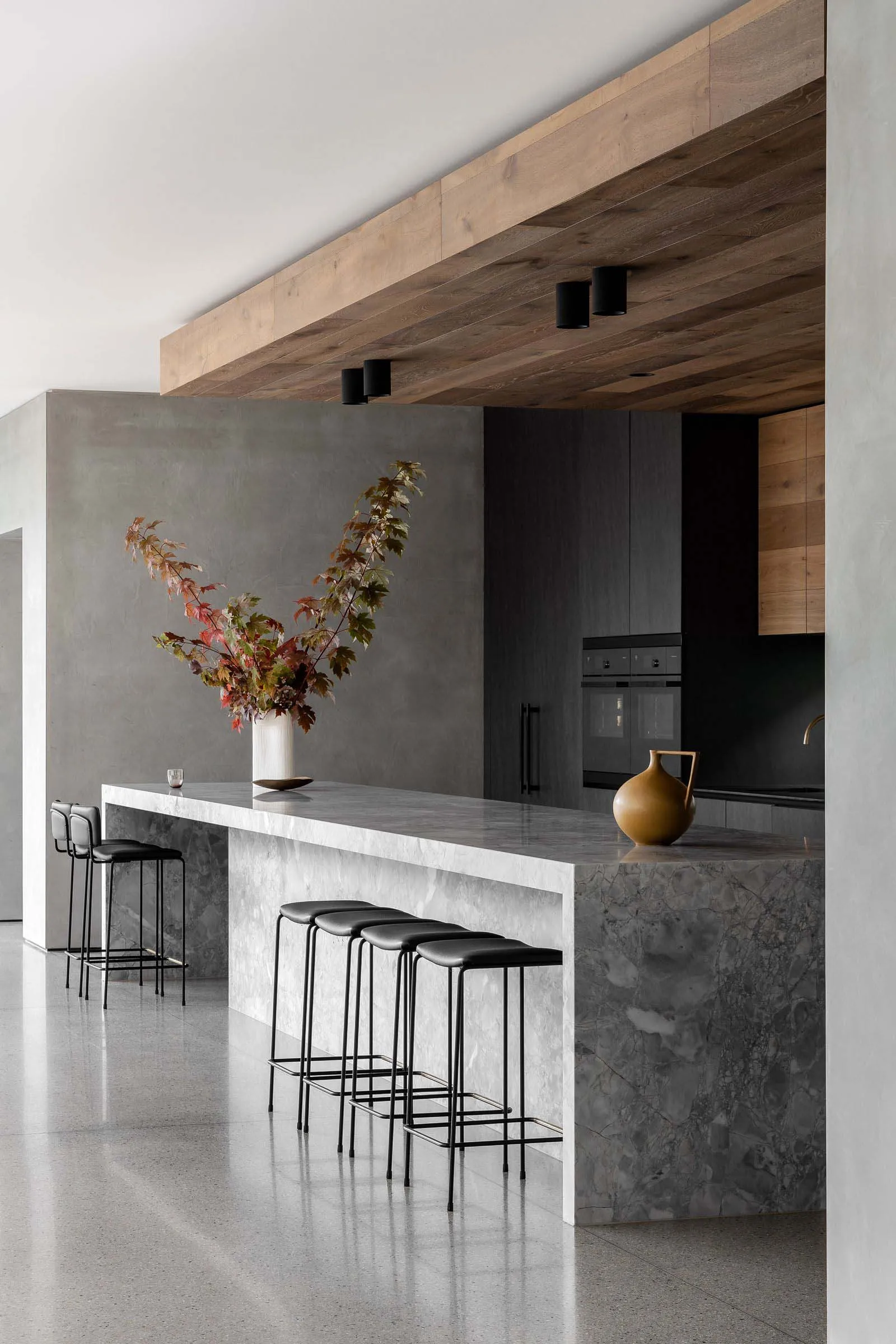 Modern kitchen with a marble island, black stools, and a large window providing natural light, featuring various appliances and a potted plant
