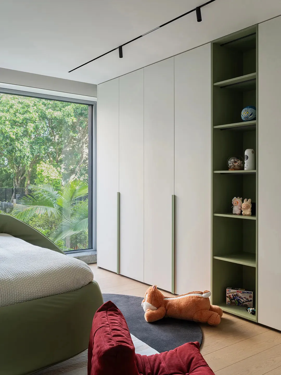 Cozy bedroom with a large bed, a chair, and two teddy bears, featuring a green theme and natural light from the window