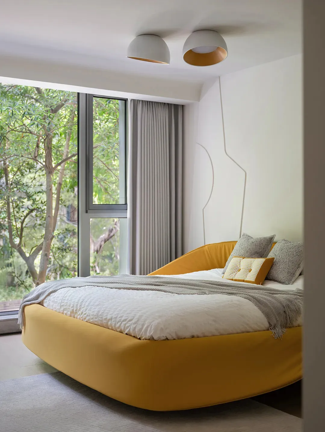A hotel bedroom with a large yellow bed, white comforter, and orange mattress, featuring two pillows and a window with natural light