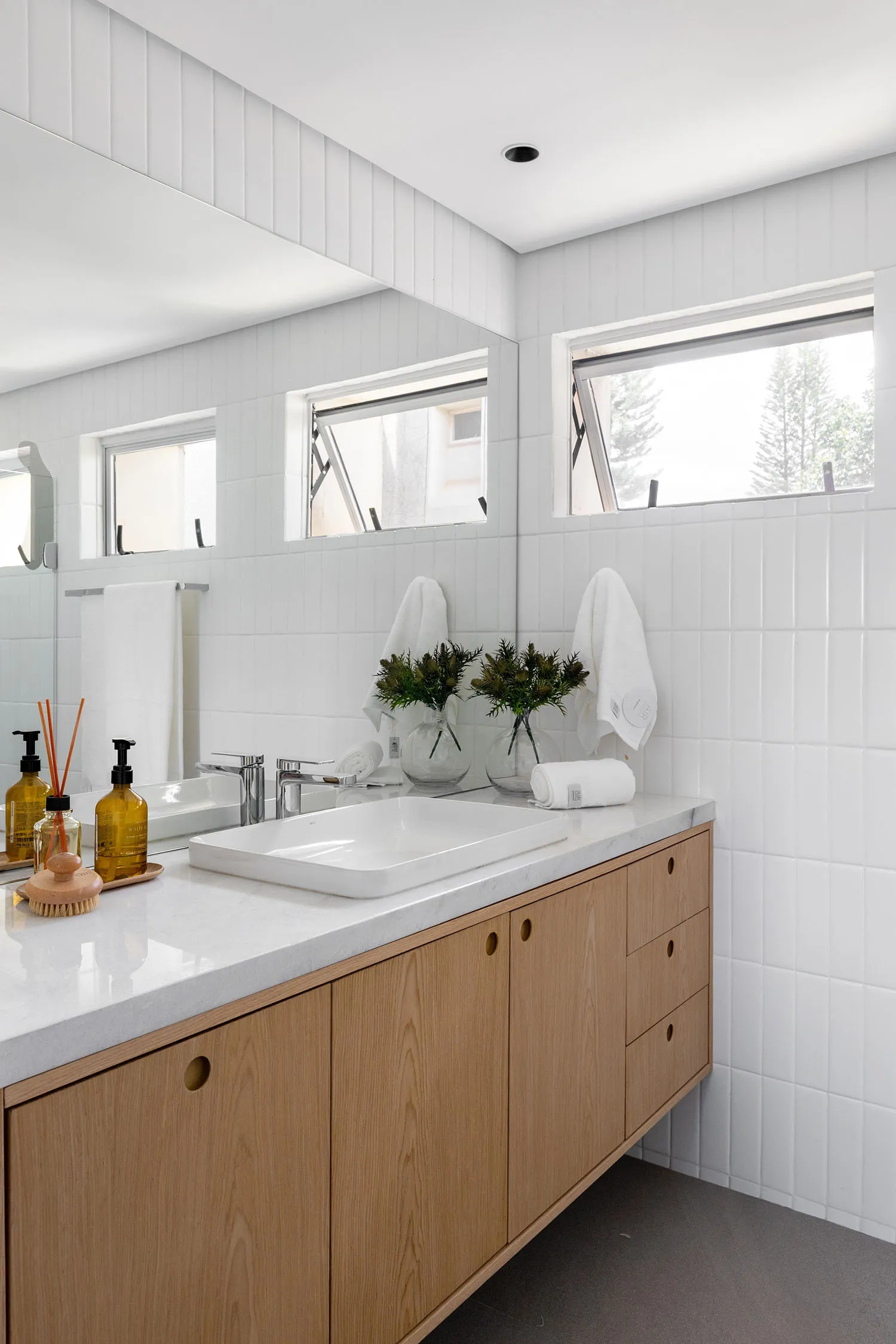 Bathroom with a white sink, mirror, and natural light from the window, featuring a clean and modern design