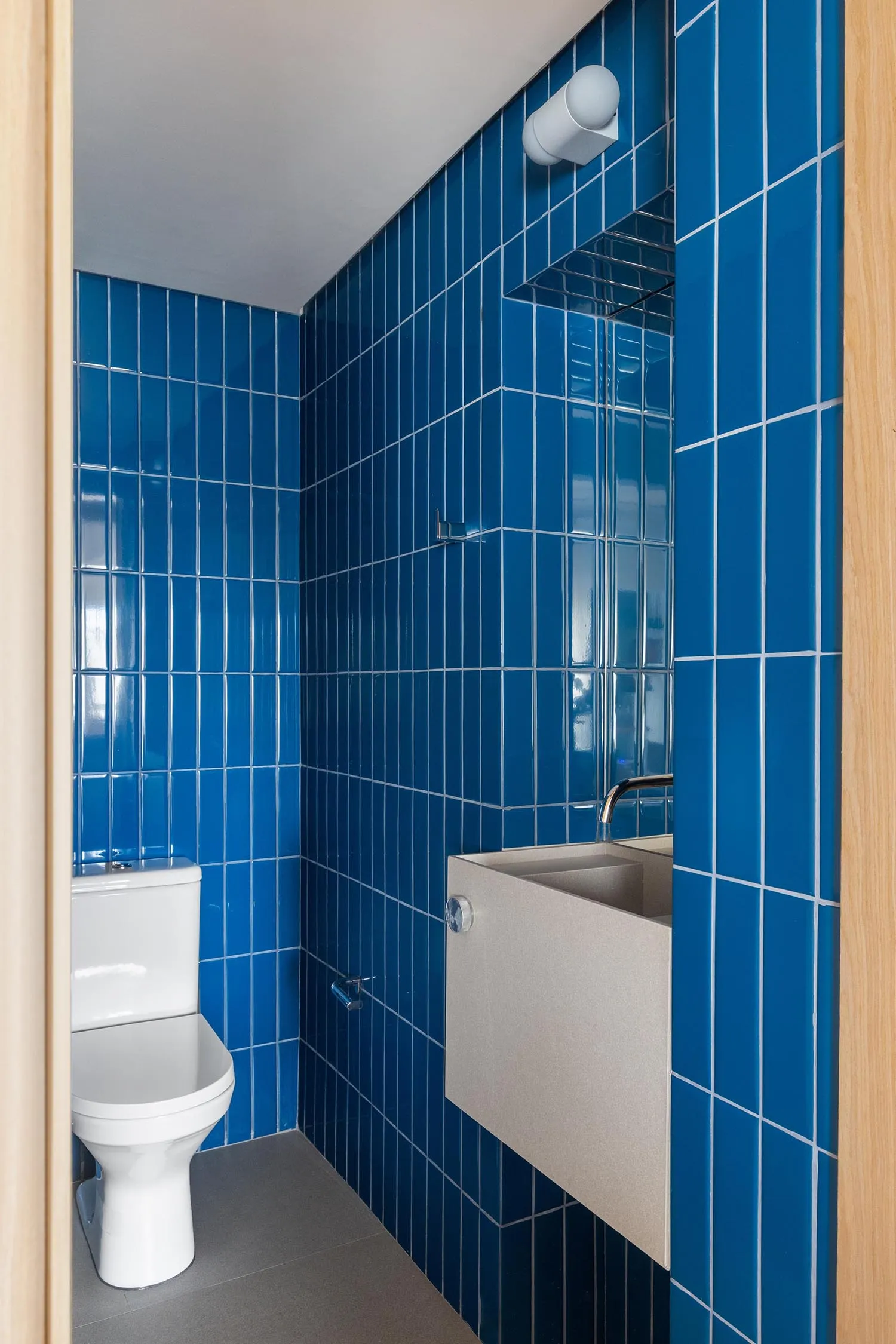 Bathroom with blue tiles, a white toilet, and two sinks, one with a cupboard underneath, in a modern and clean design