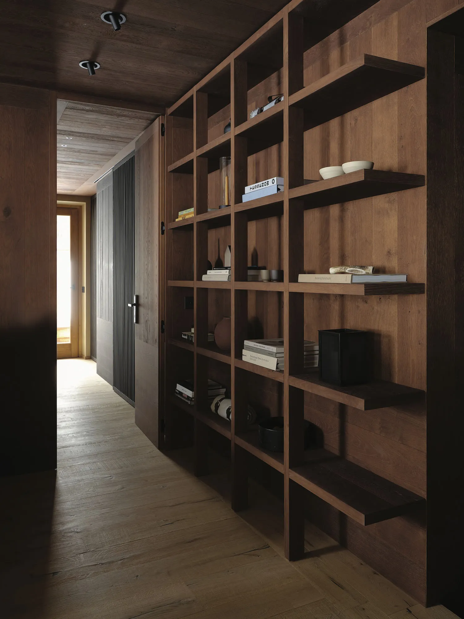A wooden bookshelf in a home with books, vases, and bowls on the shelves, creating a cozy and inviting atmosphere