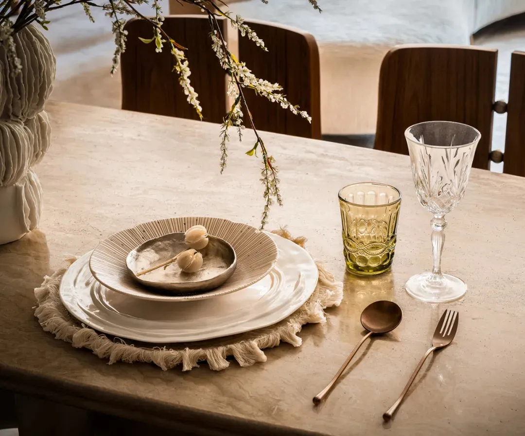 A dining table with wine glasses, cups, a bowl, and a spoon, surrounded by three chairs