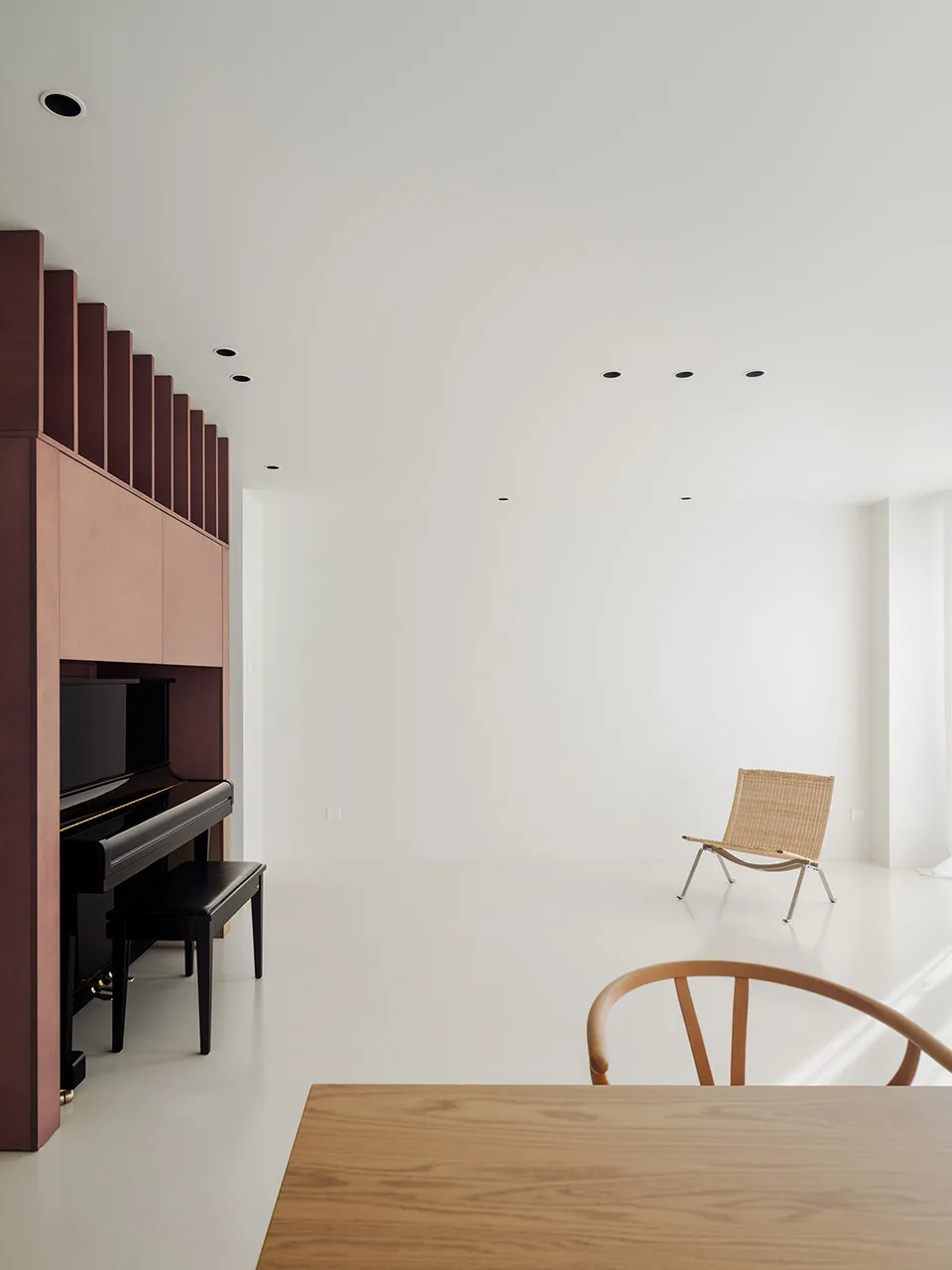 Empty living room with white walls and hardwood floors, featuring a piano, two chairs, and a dining table
