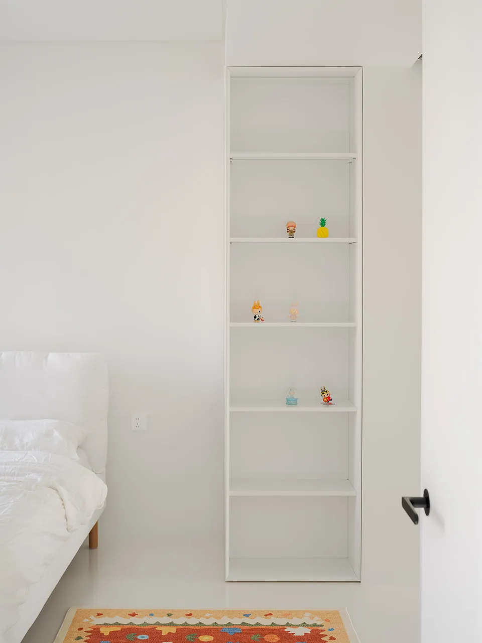 A well-organized bedroom with a large bookshelf filled with books, figurines, and decorative objects, creating an inviting atmosphere