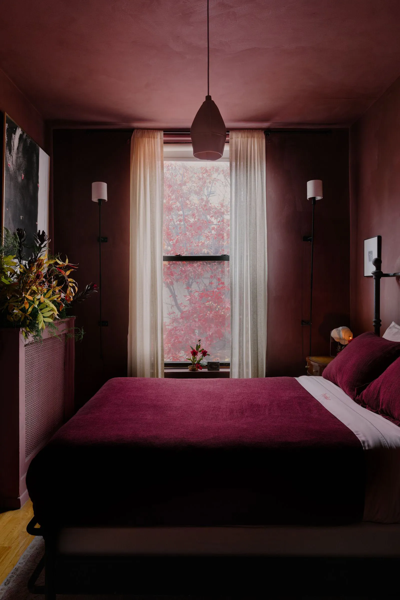 Cozy bedroom with a large bed, red walls, potted plants, and a vase, creating a warm and inviting atmosphere