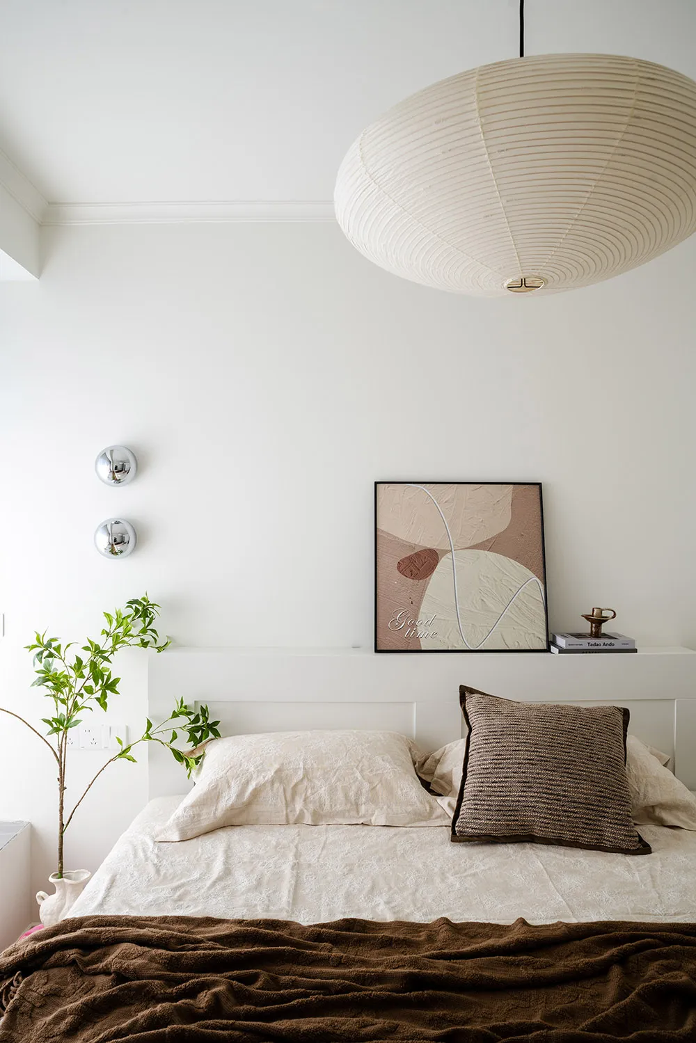A calm bedroom with a white bed, two potted plants, and a clock on the wall