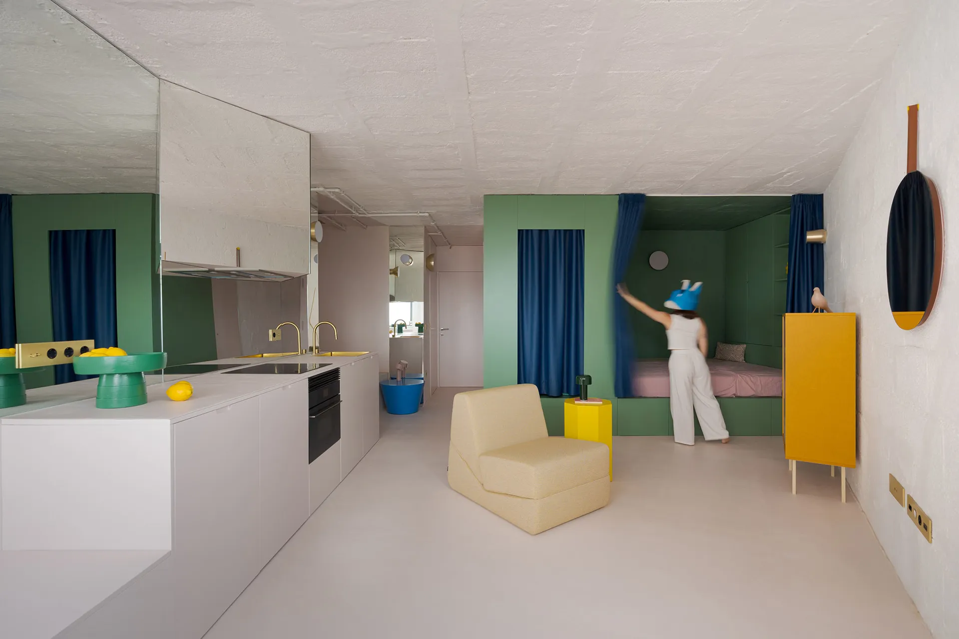 Open living area with kitchen, two couches, a chair, and a woman standing in the middle, with a bright and inviting atmosphere