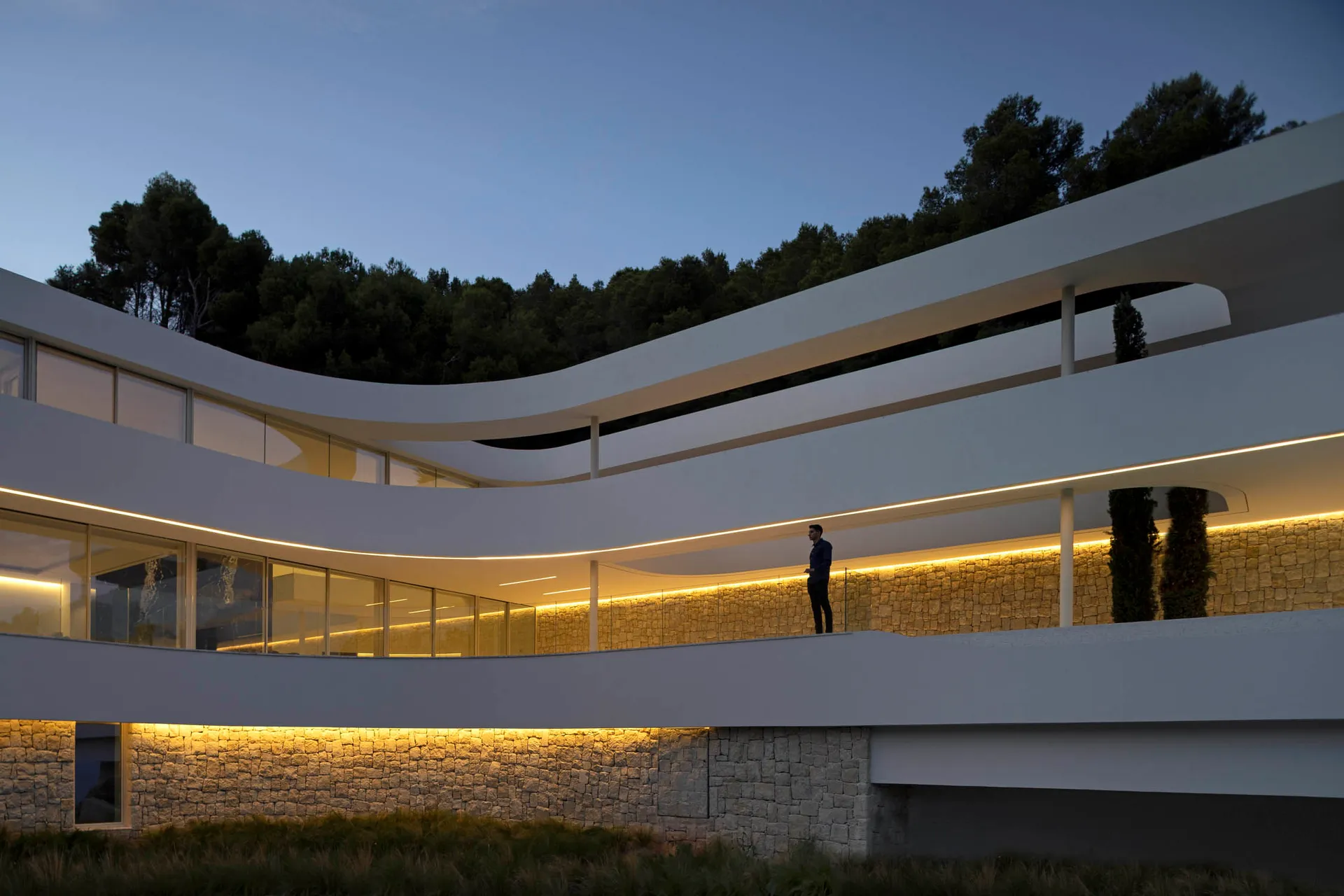 A modern building with curved walls and a stone facade, featuring multiple windows and a contemporary design