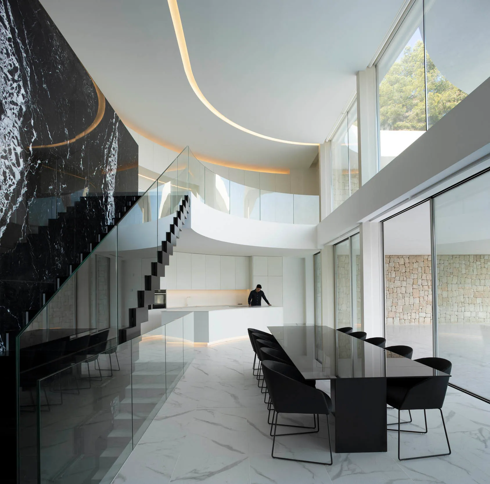 Open modern living space with a black table, two chairs, and a kitchen area with a sink, giving off a sleek and modern vibe