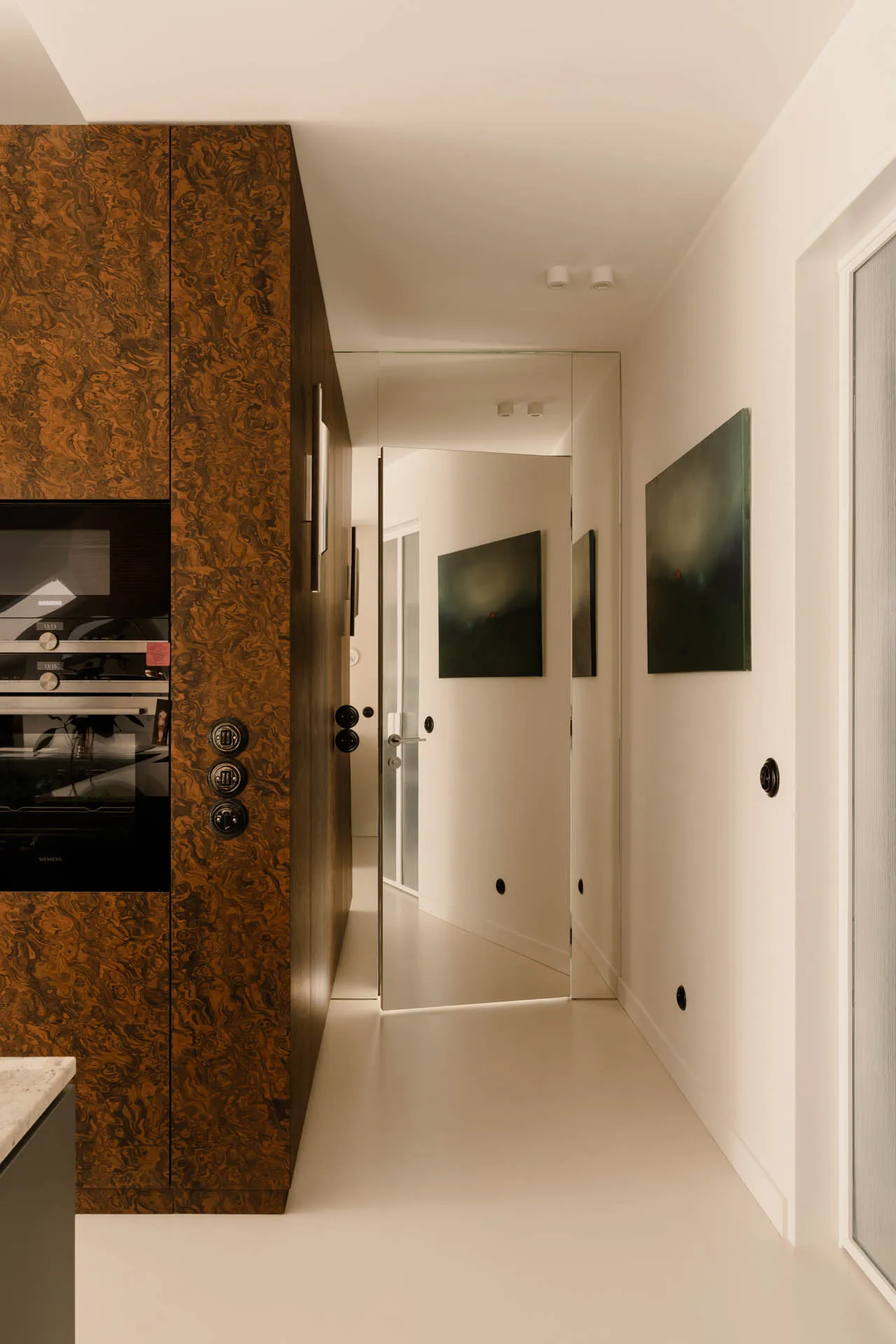 A clean and bright hallway with white walls and flooring, featuring three framed pictures and a microwave near one of the doors
