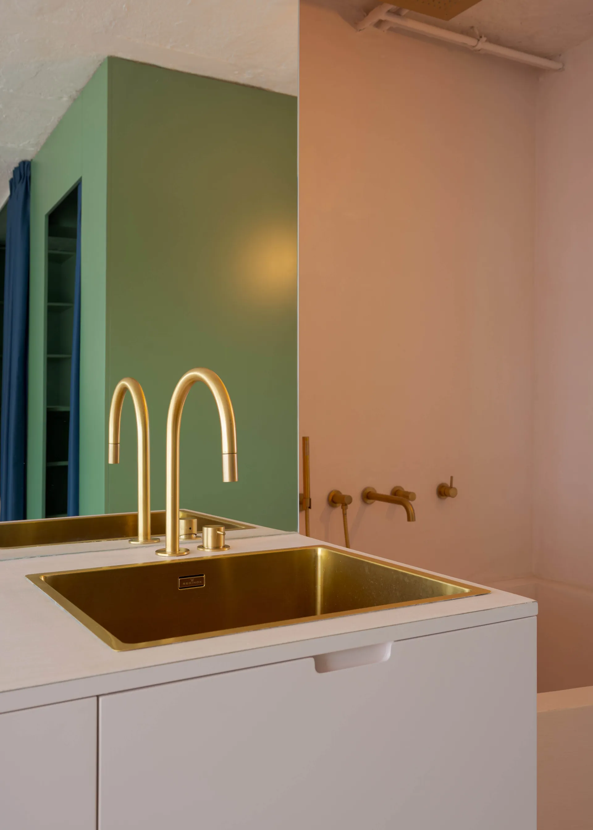 Bathroom with a gold sink, pink wall, and two bottles near the sink, creating a clean and well-organized space