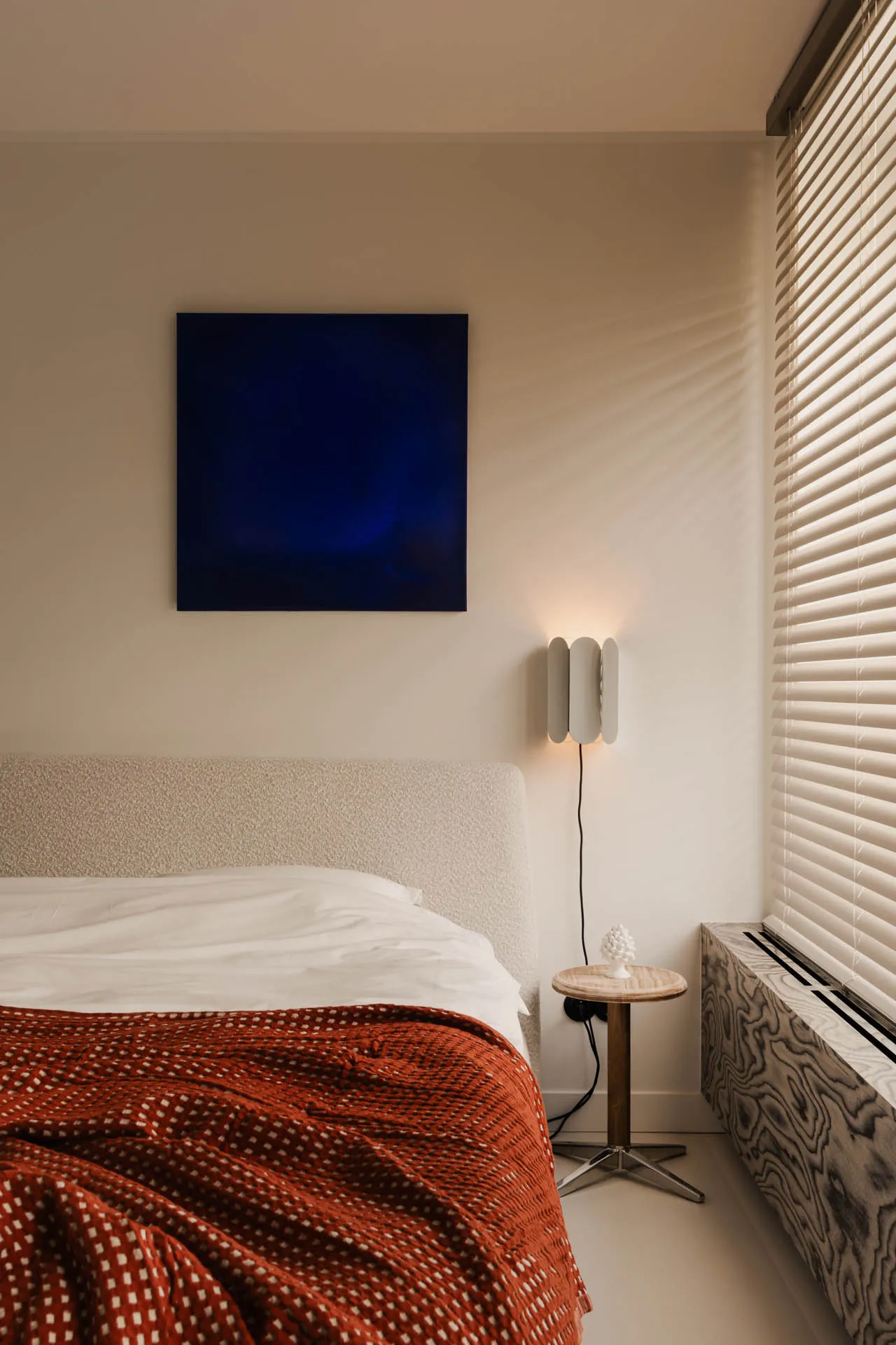 A cozy bedroom with a bed, two lamps, and a painting above the bed, set against a neutral background
