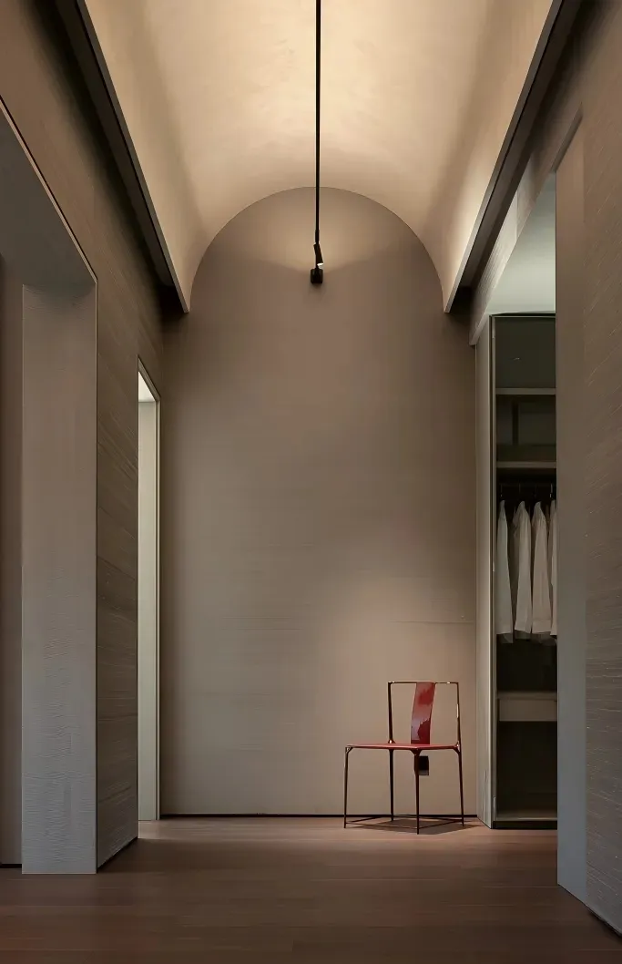 A minimalist hallway with a red chair in the center, surrounded by white walls and a single light source casting a shadow on the wall