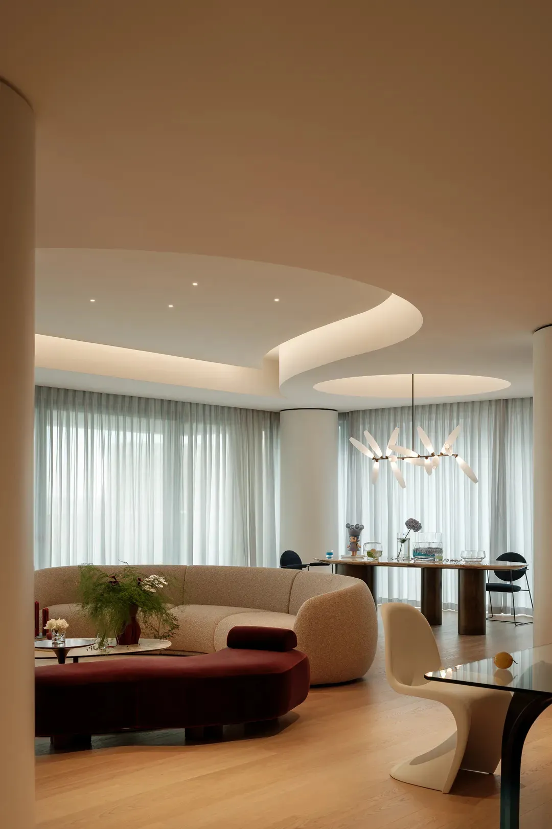A well-lit living room with a modern couch, dining table, chairs, and potted plants, set in a contemporary space with clean lines and minimalistic decoration