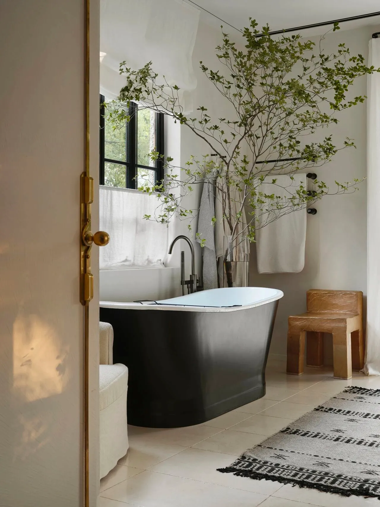 Bathroom with a freestanding tub, two windows, a potted plant, and a chair, featuring a neutral color palette and natural light