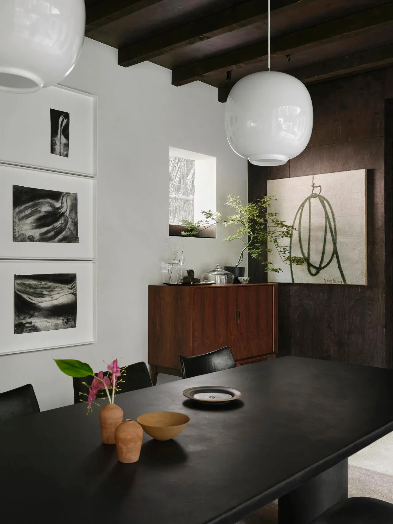 Elegant dining space with a black table, three chairs, and a potted plant, featuring a vase with flowers as a centerpiece